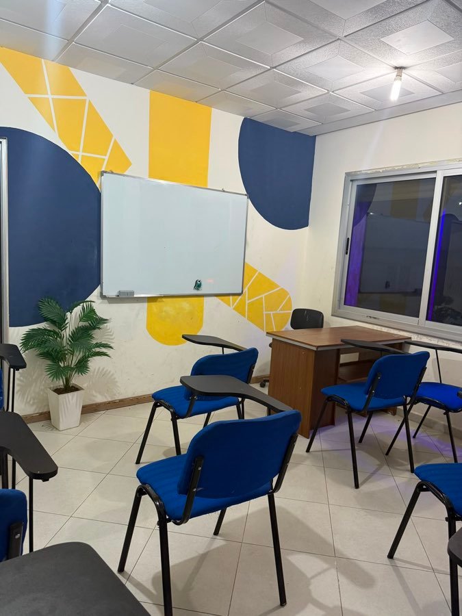 Salle lumineuse avec chaises bleues, tableau blanc et mur au motif géométrique
