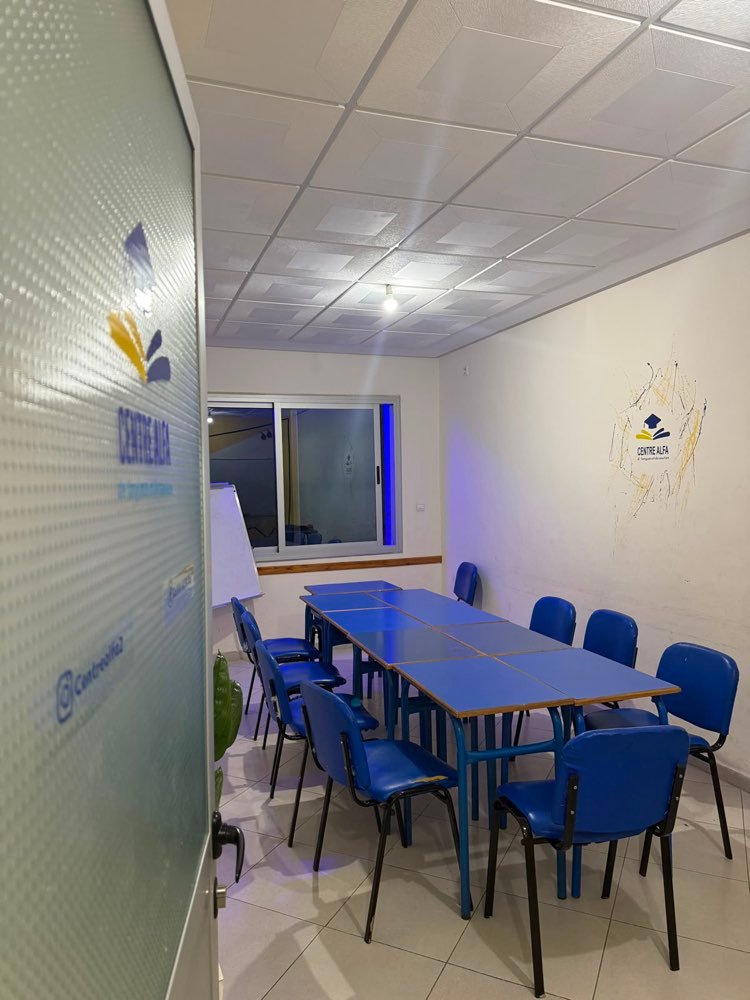 Une salle de classe lumineuse et bien équipée du Centre Alfa avec des tables bleues